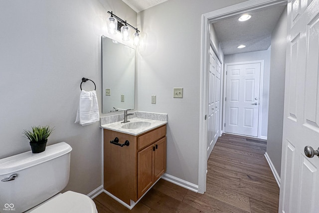 bathroom featuring baseboards, toilet, wood finished floors, a textured ceiling, and vanity