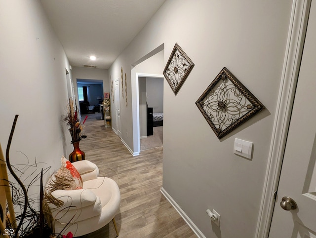 corridor with light wood finished floors, visible vents, and baseboards