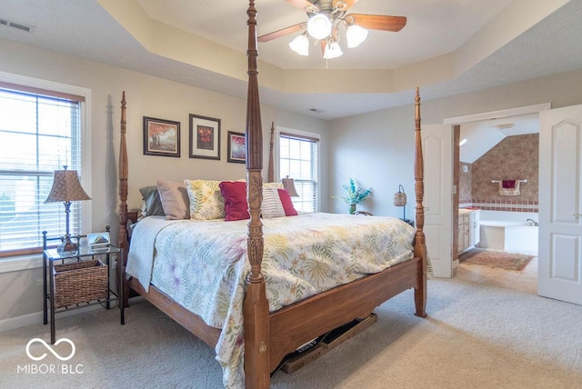 bedroom with carpet flooring, visible vents, baseboards, a raised ceiling, and ensuite bath