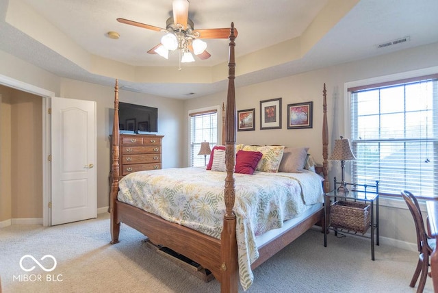 bedroom with light carpet, a tray ceiling, visible vents, and baseboards