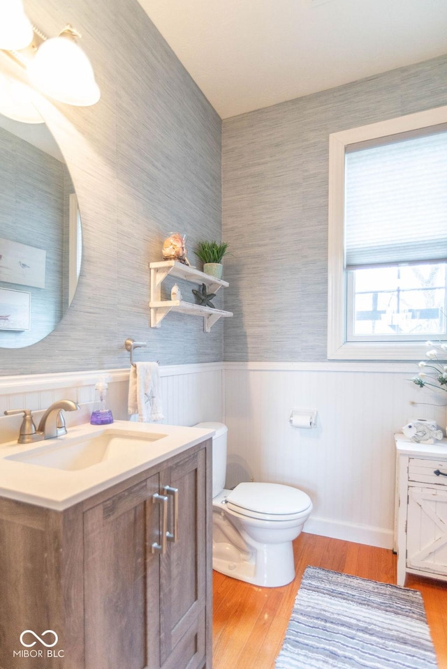 half bathroom with a wainscoted wall, vanity, toilet, and wood finished floors