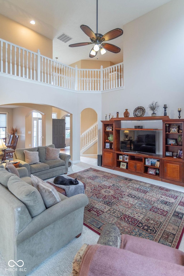 living area with a towering ceiling, visible vents, arched walkways, and ceiling fan