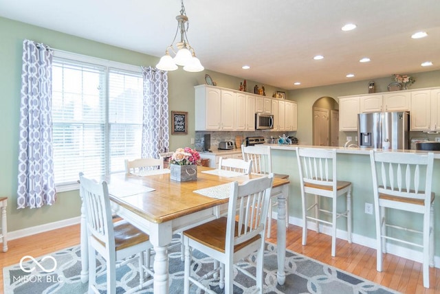 dining space with light wood-type flooring, arched walkways, baseboards, and recessed lighting