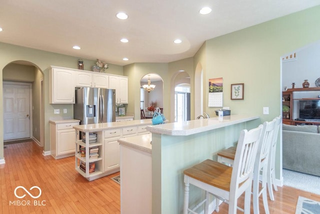 kitchen featuring arched walkways, white cabinets, stainless steel refrigerator with ice dispenser, and a kitchen breakfast bar