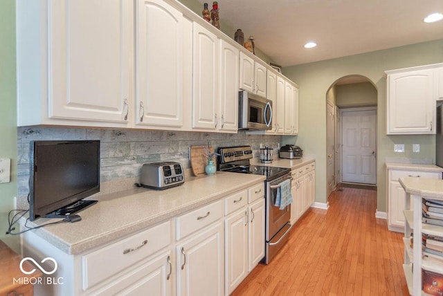 kitchen with arched walkways, stainless steel appliances, tasteful backsplash, light countertops, and white cabinets