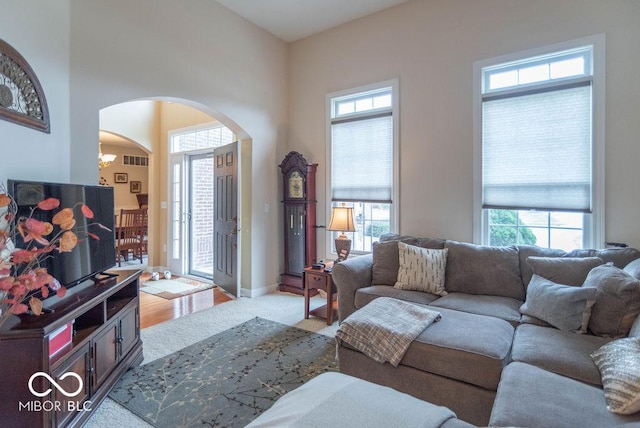 carpeted living room featuring arched walkways, visible vents, a wealth of natural light, and baseboards