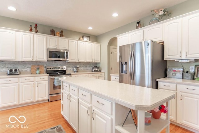 kitchen with light wood-style flooring, stainless steel appliances, white cabinets, decorative backsplash, and open shelves