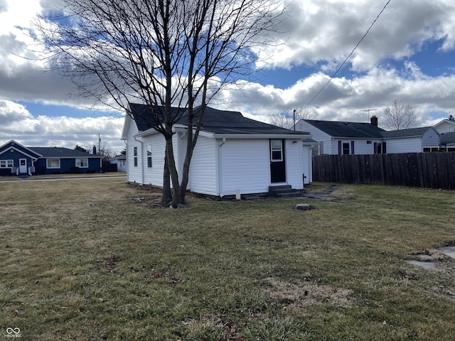 rear view of property featuring entry steps, fence, and a lawn