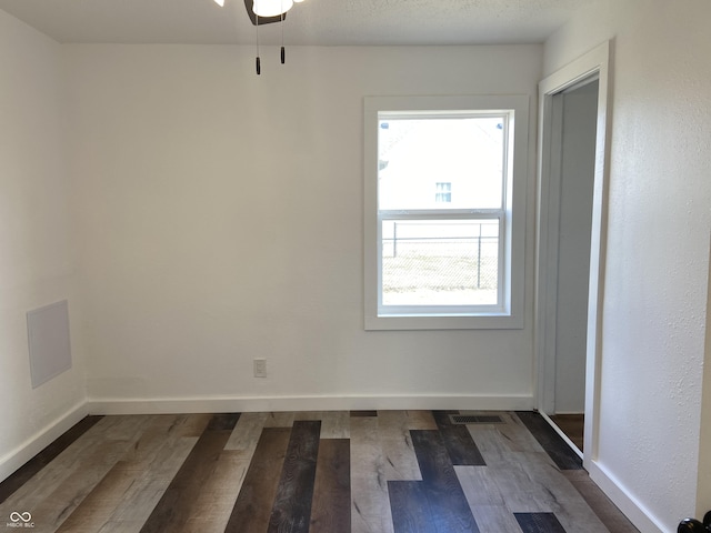 empty room with visible vents, dark wood finished floors, a textured ceiling, and baseboards