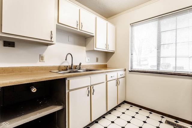 kitchen featuring light countertops, a textured ceiling, light floors, white cabinetry, and a sink