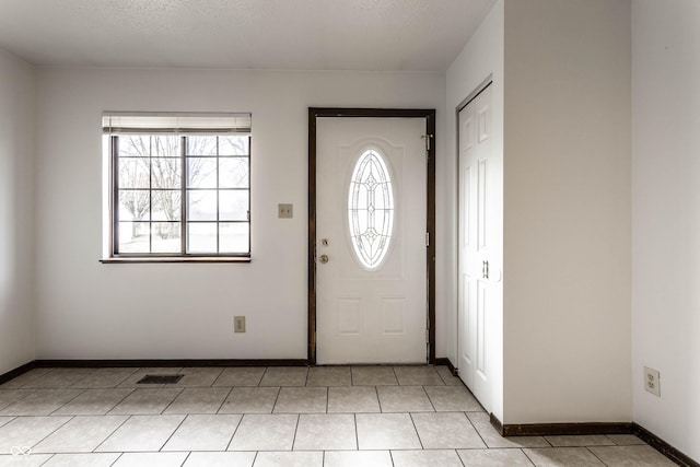 foyer entrance with light tile patterned floors, a textured ceiling, visible vents, and baseboards