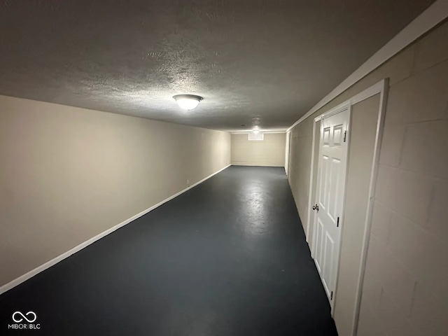 interior space with concrete block wall, a textured ceiling, and baseboards