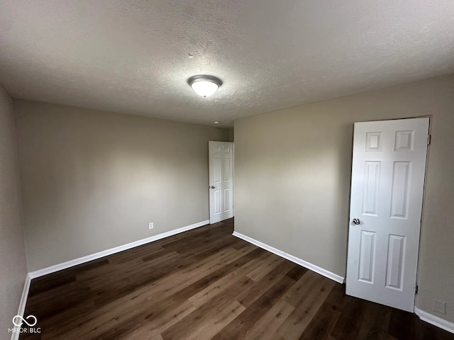 spare room with dark wood-type flooring, a textured ceiling, and baseboards