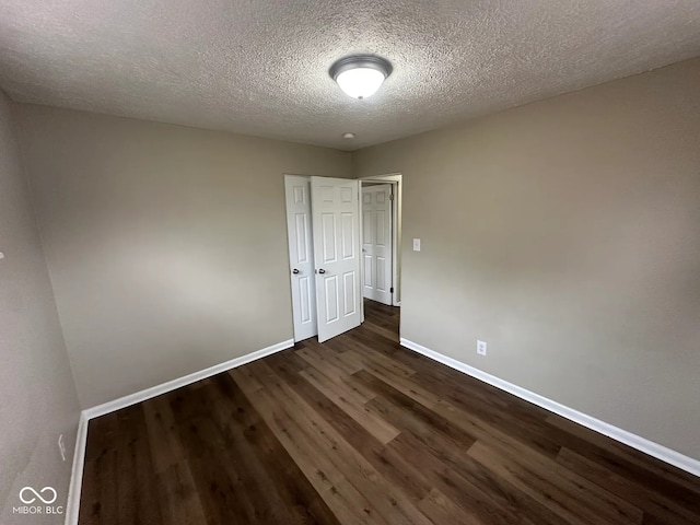 spare room with dark wood finished floors, a textured ceiling, and baseboards