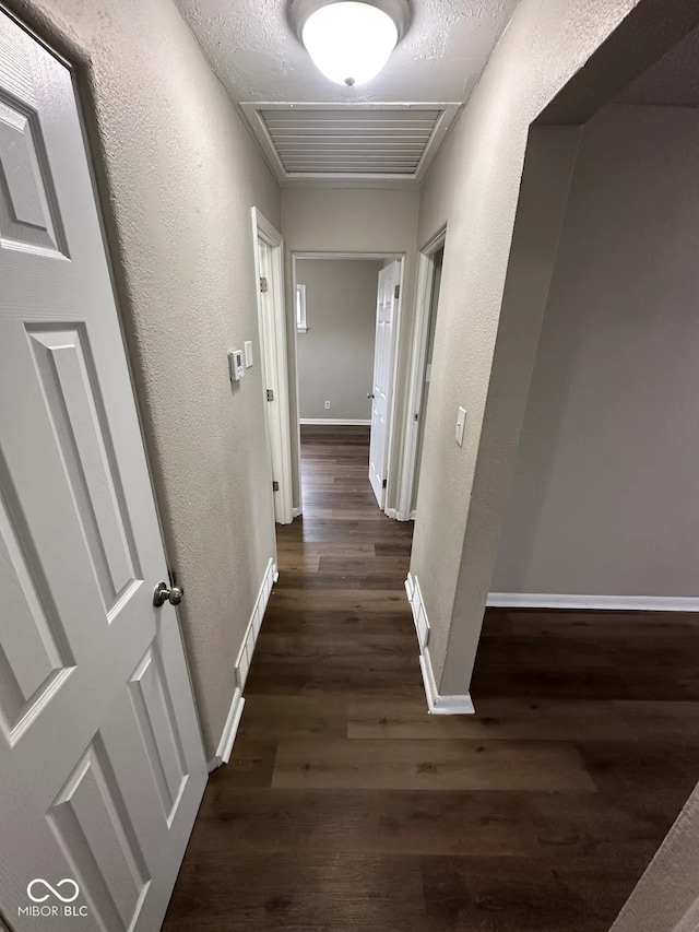 hall with baseboards, visible vents, dark wood-type flooring, and a textured wall