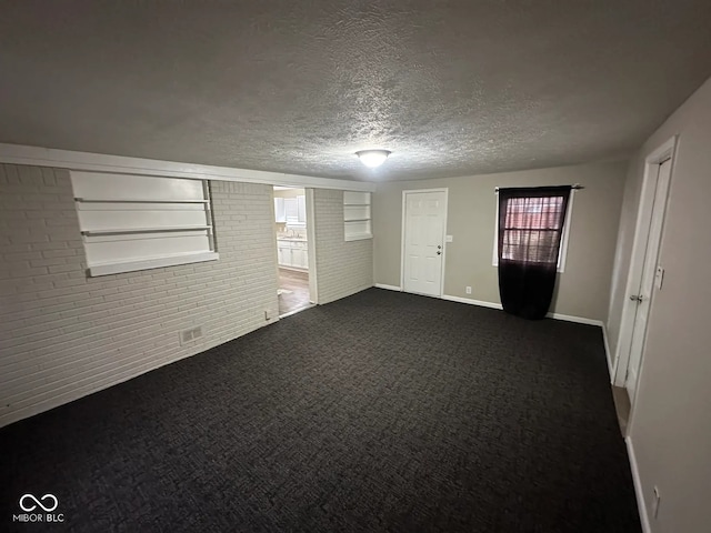 spare room with dark colored carpet, baseboards, a textured ceiling, and brick wall