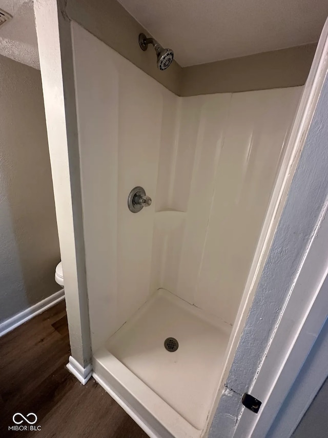 bathroom with a stall shower, wood finished floors, toilet, and baseboards