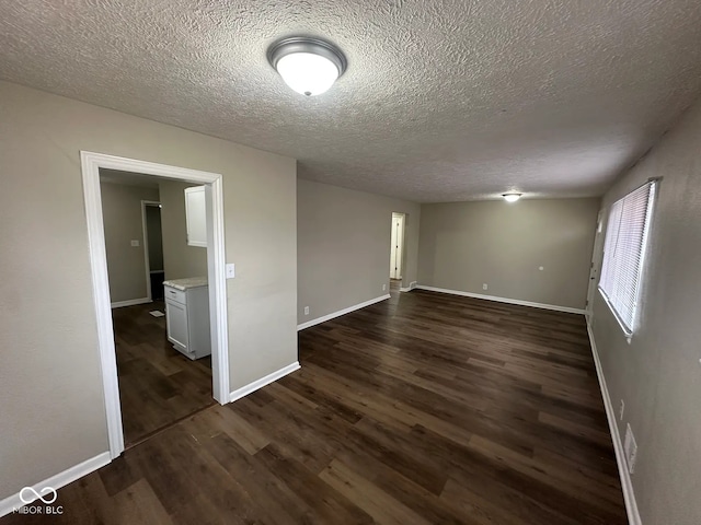 empty room featuring a textured ceiling, dark wood-type flooring, and baseboards