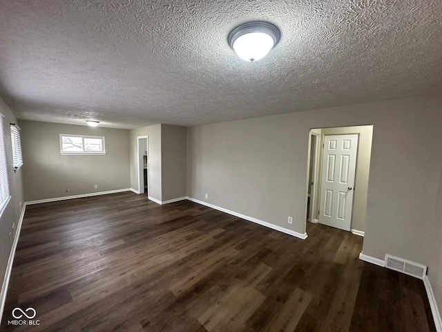 unfurnished room featuring dark wood-style flooring, visible vents, a textured ceiling, and baseboards