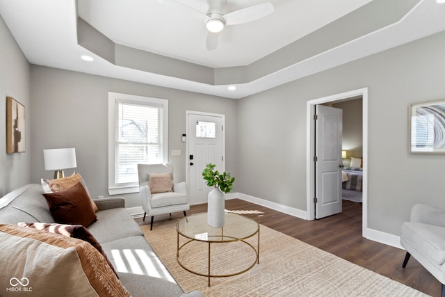 living area featuring dark wood-style flooring, recessed lighting, a raised ceiling, ceiling fan, and baseboards