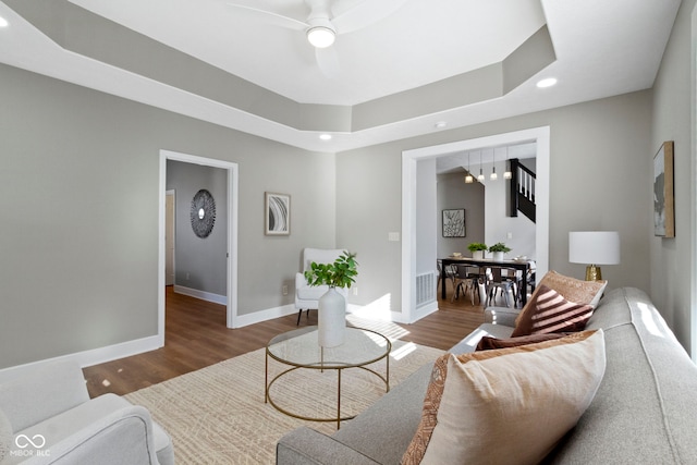 living area featuring a tray ceiling, visible vents, a ceiling fan, wood finished floors, and baseboards