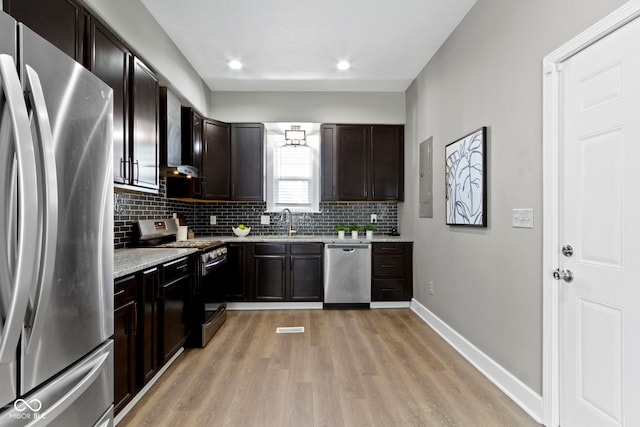 kitchen featuring stainless steel appliances, light wood-style flooring, decorative backsplash, a sink, and baseboards