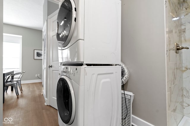 washroom featuring laundry area, wood finished floors, stacked washer and clothes dryer, and baseboards