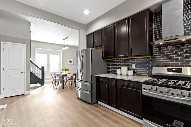 kitchen with dark brown cabinetry, tasteful backsplash, stainless steel appliances, light wood-type flooring, and wall chimney range hood