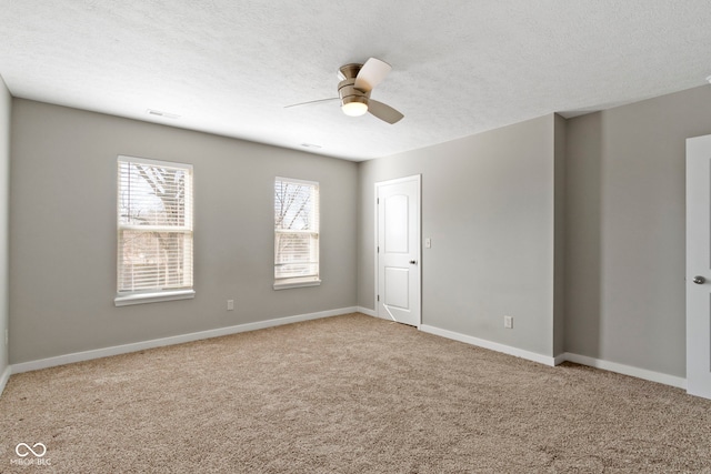 spare room featuring visible vents, light colored carpet, a ceiling fan, a textured ceiling, and baseboards