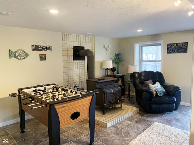 recreation room featuring a wood stove, baseboards, visible vents, and a textured ceiling