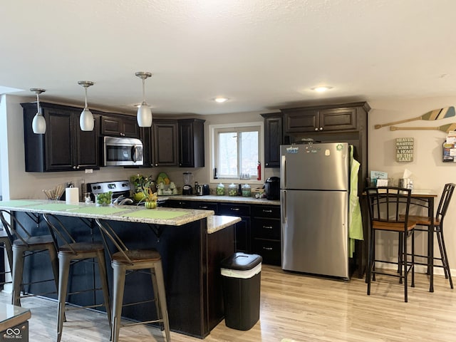 kitchen featuring a breakfast bar, a peninsula, hanging light fixtures, appliances with stainless steel finishes, and light wood-type flooring