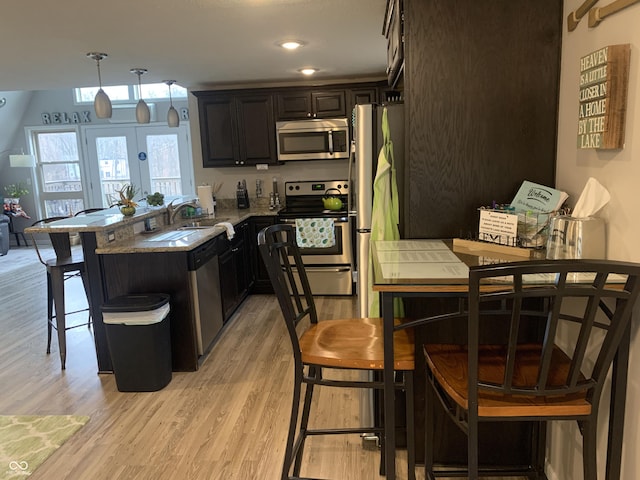 kitchen featuring a breakfast bar, a peninsula, light wood-style flooring, a sink, and appliances with stainless steel finishes