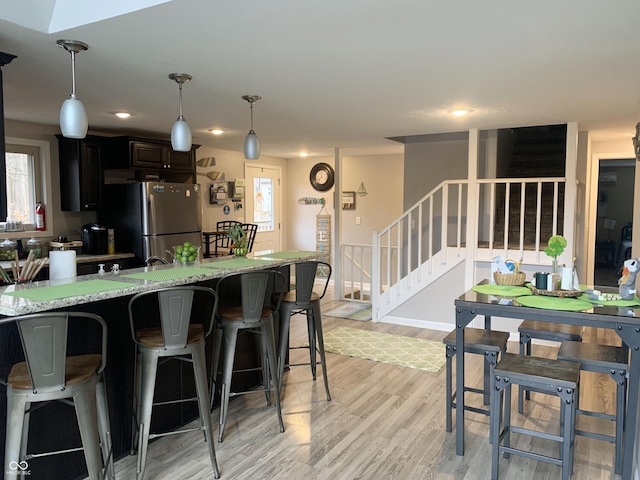 kitchen featuring decorative light fixtures, light wood-type flooring, a wealth of natural light, a kitchen breakfast bar, and freestanding refrigerator