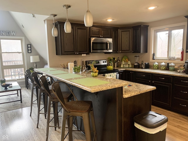 kitchen featuring a kitchen bar, a wealth of natural light, light wood-style flooring, and appliances with stainless steel finishes