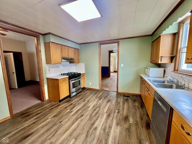 kitchen with appliances with stainless steel finishes, wood finished floors, light countertops, under cabinet range hood, and a sink