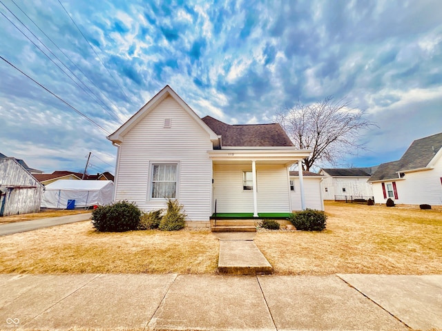 view of front of property with roof with shingles, a porch, and a front yard