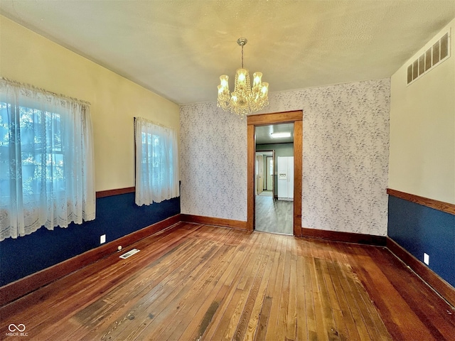 spare room with a notable chandelier, hardwood / wood-style floors, visible vents, and wallpapered walls