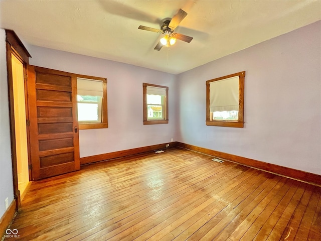 spare room with wood-type flooring, visible vents, ceiling fan, and baseboards