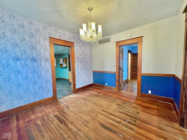 unfurnished room featuring visible vents, hardwood / wood-style floors, a chandelier, baseboards, and wallpapered walls