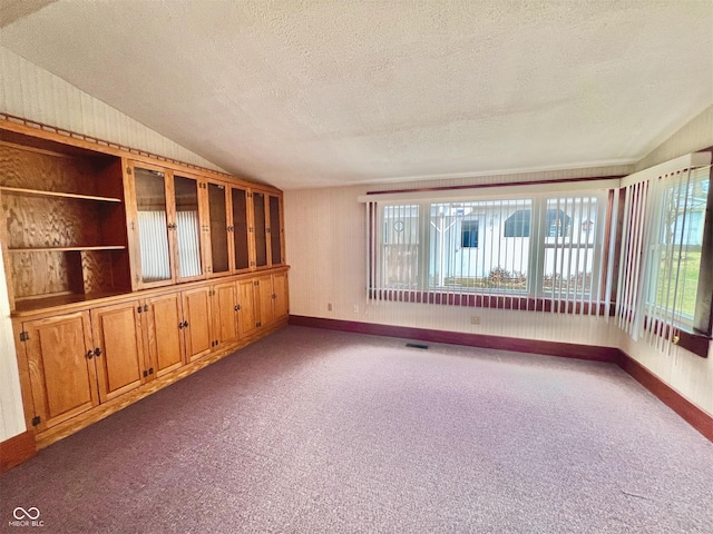 empty room with lofted ceiling, carpet flooring, visible vents, and a textured ceiling