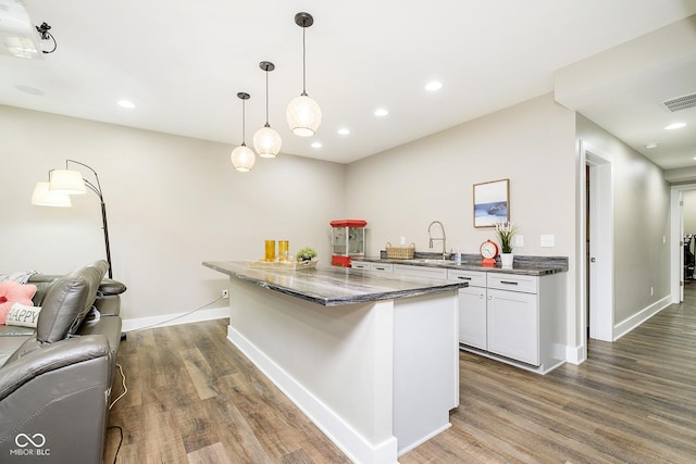 kitchen featuring visible vents, a sink, open floor plan, wood finished floors, and white cabinetry