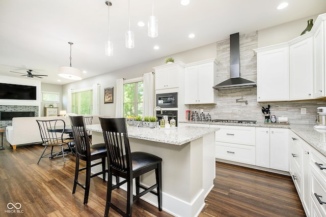 kitchen featuring ceiling fan, stainless steel appliances, wall chimney range hood, open floor plan, and backsplash