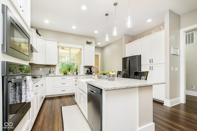 kitchen featuring oven, built in microwave, an island with sink, black fridge, and stainless steel dishwasher