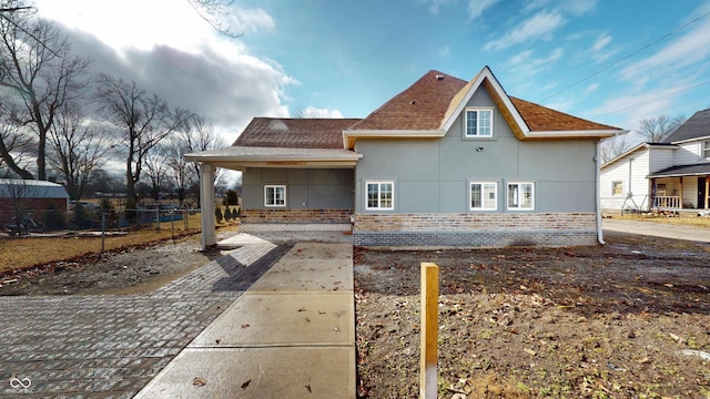 view of front of property with brick siding, roof with shingles, fence, and stucco siding