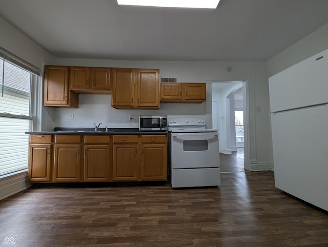 kitchen with white appliances, dark wood finished floors, brown cabinetry, dark countertops, and a sink