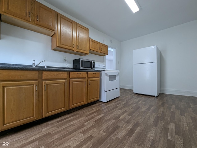 kitchen with dark countertops, white appliances, baseboards, and dark wood-style floors