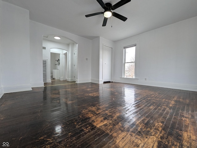 empty room featuring hardwood / wood-style flooring, baseboards, arched walkways, and a ceiling fan