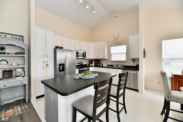 kitchen featuring dark countertops, rail lighting, appliances with stainless steel finishes, white cabinetry, and a kitchen breakfast bar