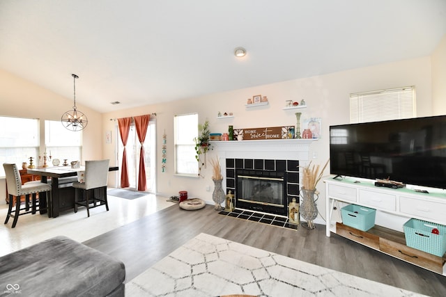 living room with vaulted ceiling, a fireplace, wood finished floors, and a notable chandelier