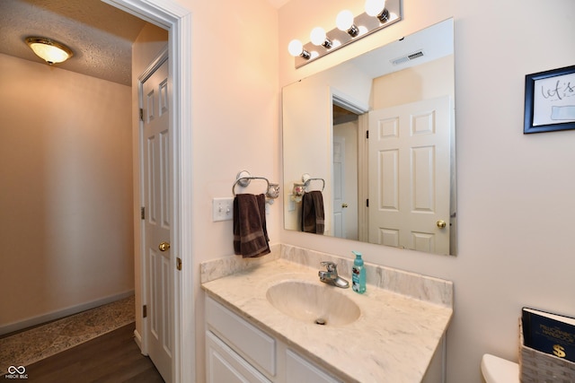 bathroom with visible vents, toilet, vanity, a textured ceiling, and wood finished floors